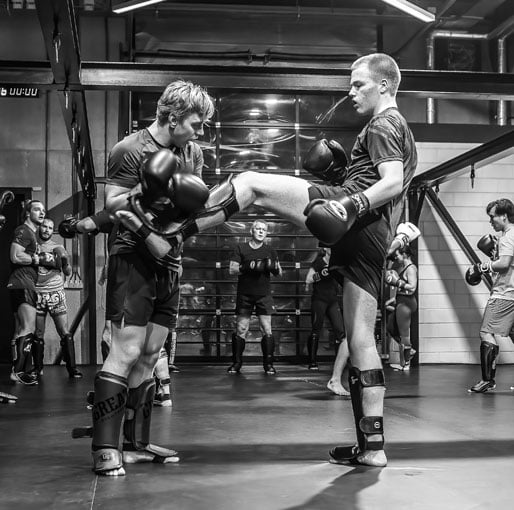 twee mannen tijdens een kickboksles. de ene man voert een kick uit bij de andere man.